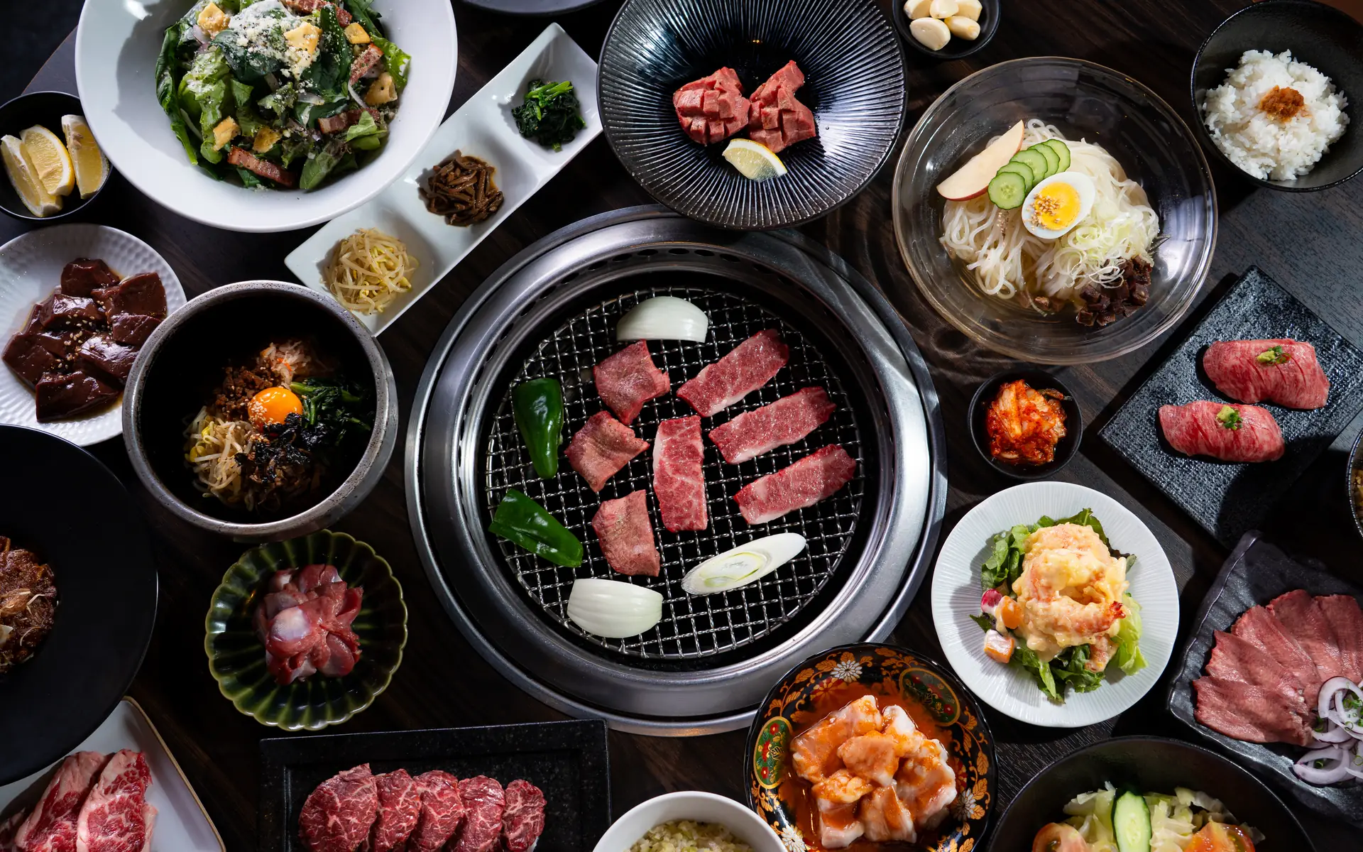 焼き網を囲むように、カルビや牛タン、冷麺、サラダが並ぶテーブル